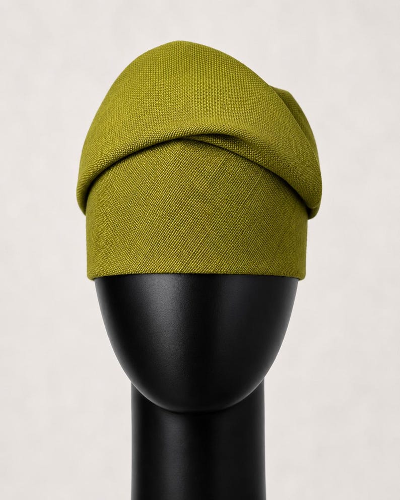 Peut inclure: Un chapeau vert chartreuse avec un design pli&eacute;, pr&eacute;sent&eacute; sur une t&ecirc;te de mannequin noire. Le chapeau a un tissu textur&eacute; et une forme arrondie, avec une bande autour de la base. Le fond est blanc cass&eacute; uni.
