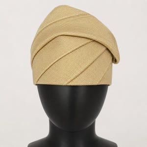 Peut inclure: Un chapeau beige avec un design pli&eacute; unique. Le chapeau pr&eacute;sente des d&eacute;tails diagonaux et c&ocirc;tel&eacute;s, cr&eacute;ant un aspect textur&eacute;. Il est pr&eacute;sent&eacute; sur une t&ecirc;te de mannequin noire, mettant en valeur sa forme et son style. Ce couvre-chef convient &agrave; diverses occasions.