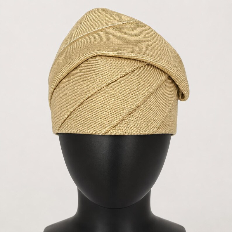 Peut inclure: Un chapeau beige avec un design pli&eacute; unique. Le chapeau pr&eacute;sente des d&eacute;tails diagonaux et c&ocirc;tel&eacute;s, cr&eacute;ant un aspect textur&eacute;. Il est pr&eacute;sent&eacute; sur une t&ecirc;te de mannequin noire, mettant en valeur sa forme et son style. Ce couvre-chef convient &agrave; diverses occasions.