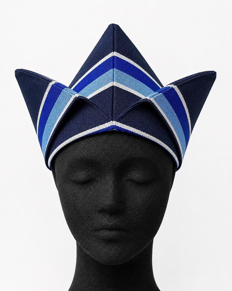 May include: A navy blue, peaked hat with a geometric design. The hat features alternating stripes of white, light blue, and dark blue. The hat is displayed on a black mannequin head.