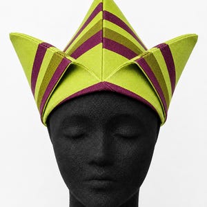 May include: A lime green and purple striped hat with a geometric design. The hat is worn on a black mannequin head. The hat's design features a series of angled panels, creating a unique and eye-catching shape. The stripes are evenly spaced and run horizontally.
