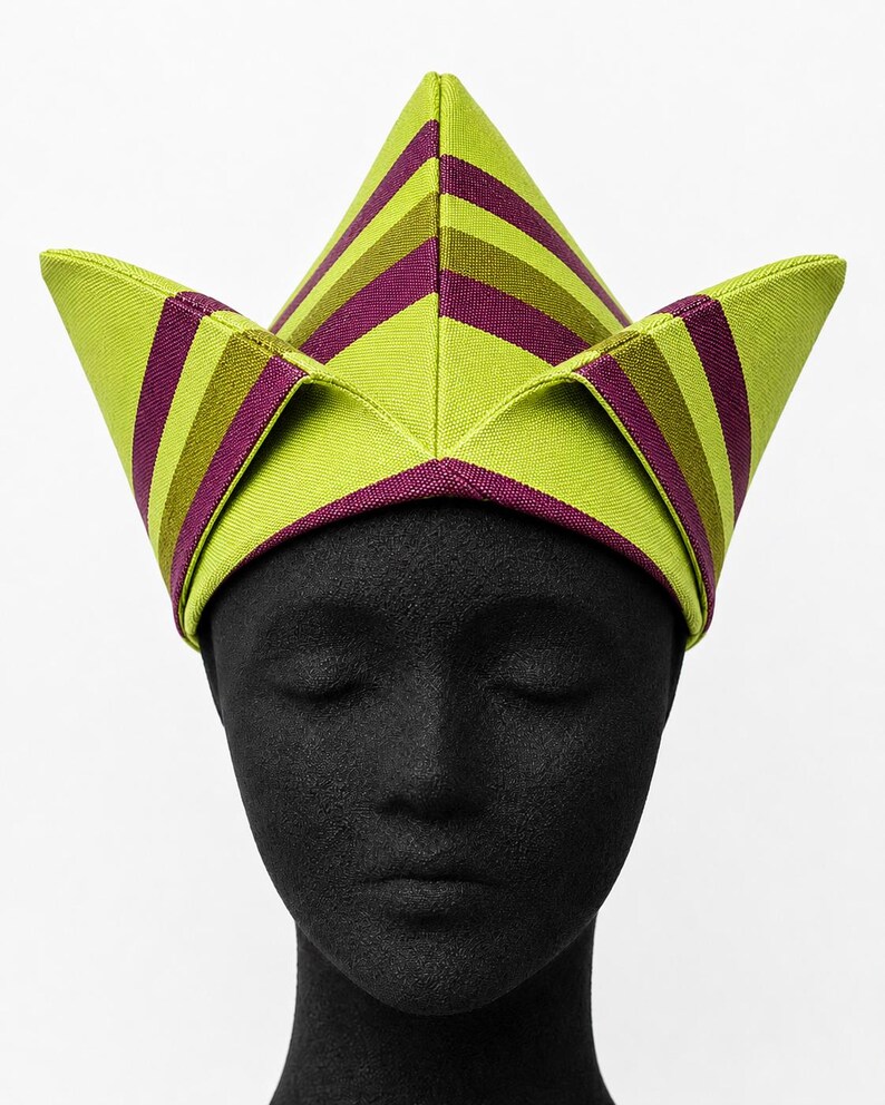 May include: A lime green and purple striped hat with a geometric design. The hat is worn on a black mannequin head. The hat's design features a series of angled panels, creating a unique and eye-catching shape. The stripes are evenly spaced and run horizontally.