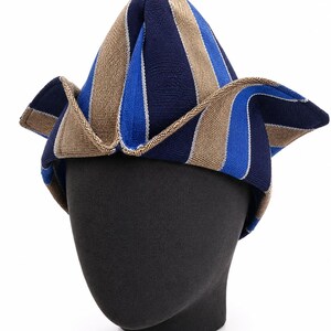 May include: A striped hat in navy blue, light blue, and tan, displayed on a black mannequin head. The hat has a unique, pointed shape with a wide, folded brim. The stripes run vertically, creating a bold pattern.