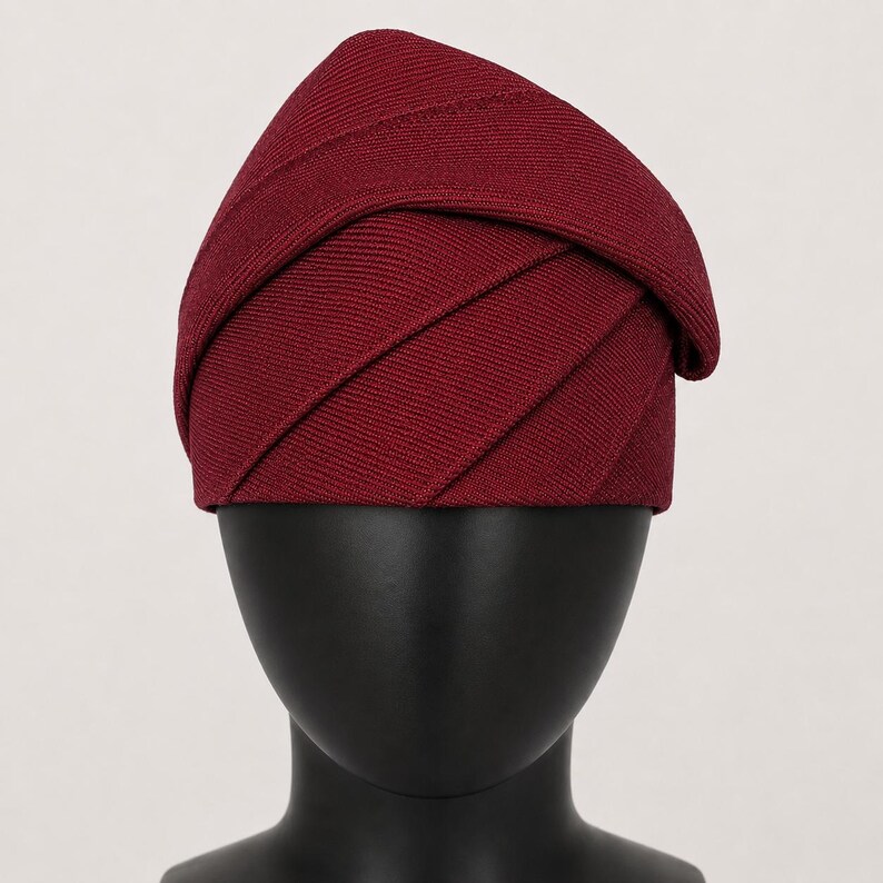 Peut inclure: Un chapeau bordeaux au design superpos&eacute; unique. Le tissu est c&ocirc;tel&eacute;, cr&eacute;ant un aspect textur&eacute;. Le chapeau est pr&eacute;sent&eacute; sur une t&ecirc;te de mannequin noire, mettant en valeur sa forme et son style. Ce couvre-chef est adapt&eacute; aux occasions sp&eacute;ciales.