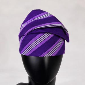 Peut inclure: Un turban &agrave; rayures violettes et blanches. Le tissu est pli&eacute; et drap&eacute; pour cr&eacute;er un couvre-chef &eacute;l&eacute;gant. Les rayures sont un m&eacute;lange de violet et de blanc, cr&eacute;ant un motif visuellement attrayant. Le turban est pr&eacute;sent&eacute; sur une t&ecirc;te de mannequin noire.