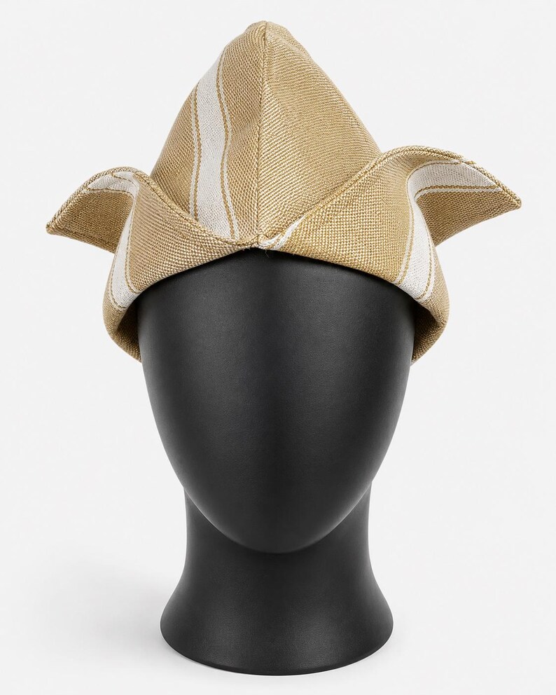 May include: A tan and white striped hat with a unique, angular design. The hat is displayed on a black mannequin head, showcasing its shape and texture. The hat's fabric appears to be woven, with a structured form.