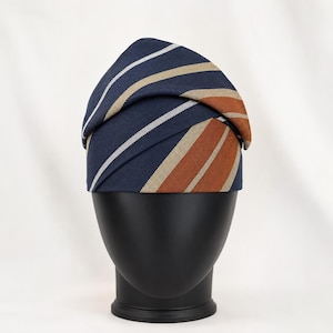Peut inclure: Un foulard de t&ecirc;te bleu marine avec des rayures blanches, beiges et orange. Le tissu est pli&eacute; et drap&eacute; sur une t&ecirc;te de mannequin noire. Le foulard est un accessoire &eacute;l&eacute;gant.