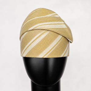 Peut inclure: Chapeau &agrave; rayures jaunes et blanches, pr&eacute;sent&eacute; sur une t&ecirc;te de mannequin noire. Le chapeau pr&eacute;sente un motif &agrave; rayures diagonales et un design pli&eacute;. Le tissu semble textur&eacute;.