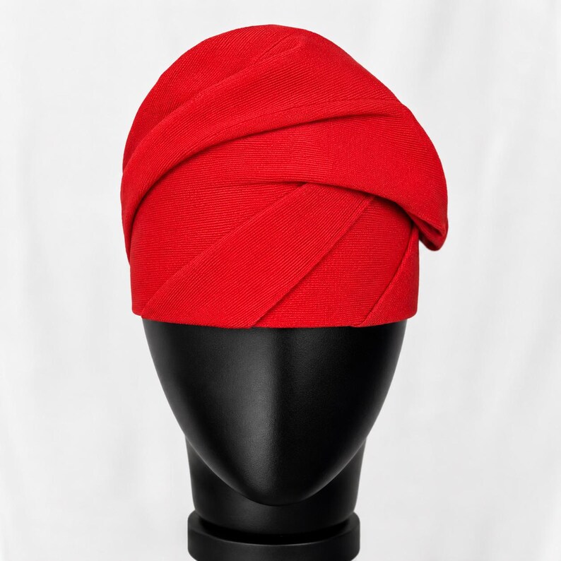 Peut inclure: Un turban rouge vif avec un design envelopp&eacute;. Le chapeau est pr&eacute;sent&eacute; sur une t&ecirc;te de mannequin noire sur fond blanc. Le tissu semble &ecirc;tre un tricot c&ocirc;tel&eacute;, ajoutant de la texture au couvre-chef.