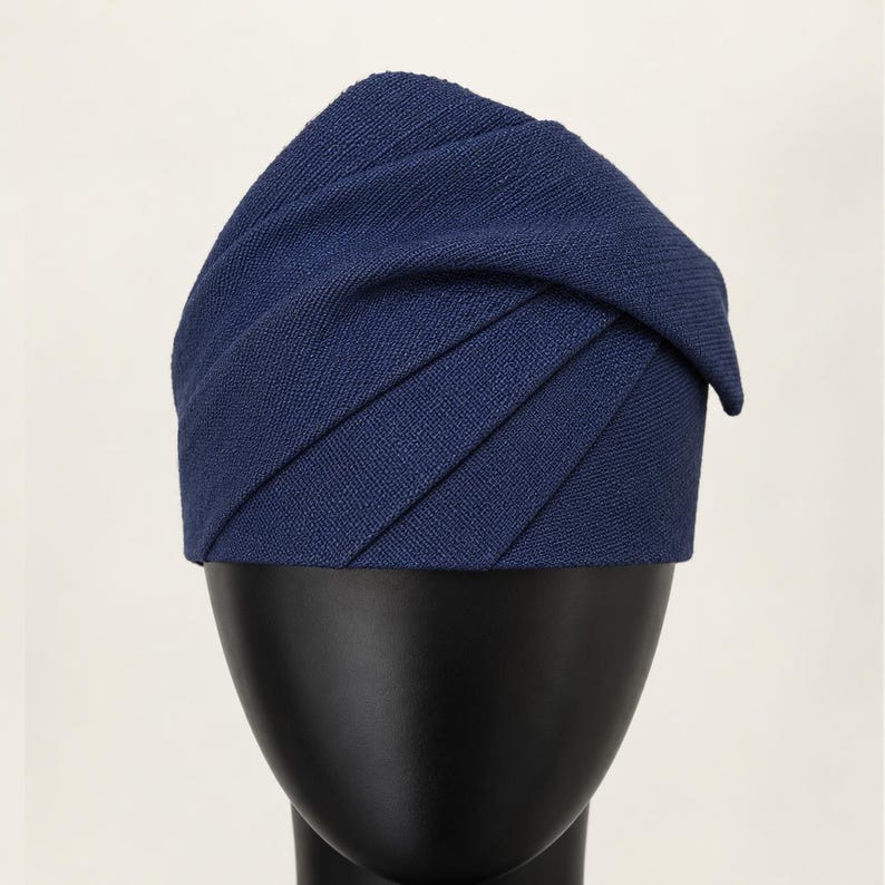 Peut inclure: Un chapeau bleu marine avec un design pliss&eacute; unique. Le tissu du chapeau est de couleur unie, et les plis cr&eacute;ent un effet textur&eacute; et superpos&eacute;. Le chapeau est pr&eacute;sent&eacute; sur une t&ecirc;te de mannequin noire, mettant en valeur sa forme et son style.
