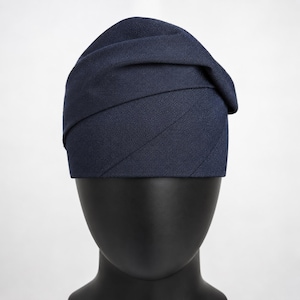Peut inclure: Un chapeau bleu marine avec un design envelopp&eacute; unique. Le chapeau est fait d'un tissu textur&eacute; et pr&eacute;sente une forme asym&eacute;trique pli&eacute;e. Le chapeau est pr&eacute;sent&eacute; sur une t&ecirc;te de mannequin noire, mettant en valeur sa forme et son style. Ce couvre-chef convient &agrave; diverses occasions.