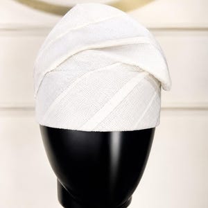 Peut inclure: Un chapeau blanc textur&eacute; avec un design unique, pr&eacute;sent&eacute; sur une t&ecirc;te de mannequin noire. Le chapeau pr&eacute;sente des rayures diagonales et un bord pli&eacute;, ce qui en fait un accessoire &eacute;l&eacute;gant.