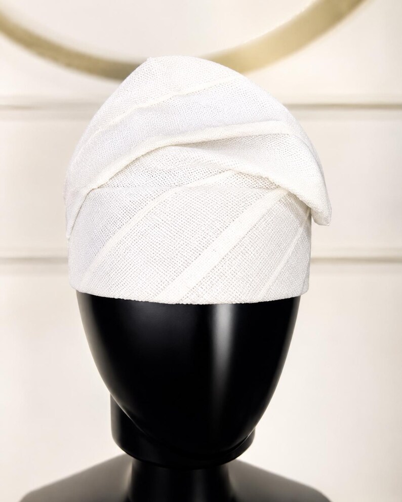 Peut inclure: Un chapeau blanc textur&eacute; avec un design unique, pr&eacute;sent&eacute; sur une t&ecirc;te de mannequin noire. Le chapeau pr&eacute;sente des rayures diagonales et un bord pli&eacute;, ce qui en fait un accessoire &eacute;l&eacute;gant.