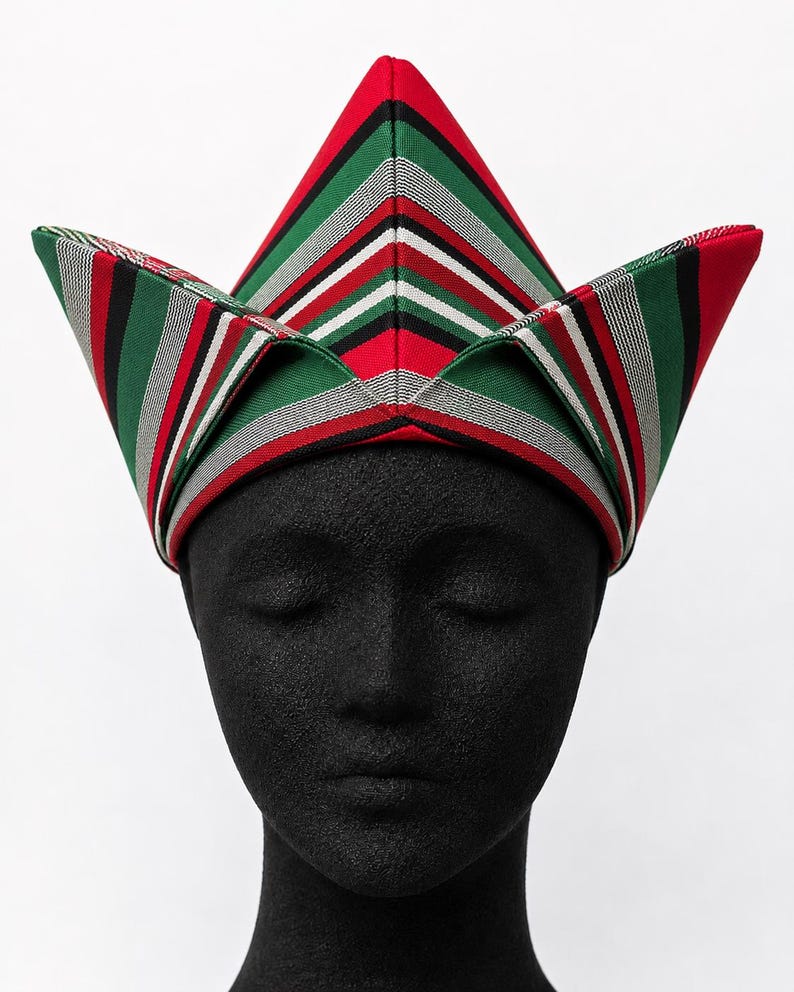 May include: A colorful, striped hat with a unique, angular design. The hat features red, green, black, white, and gray stripes. The hat is displayed on a black mannequin head against a white background.