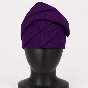 Peut inclure: Un chapeau violet fonc&eacute; avec un design superpos&eacute; unique. Le tissu du chapeau est c&ocirc;tel&eacute; et les couches cr&eacute;ent un aspect textur&eacute; et g&eacute;om&eacute;trique. Le chapeau est pr&eacute;sent&eacute; sur une t&ecirc;te de mannequin noire, mettant en valeur sa forme et son style.