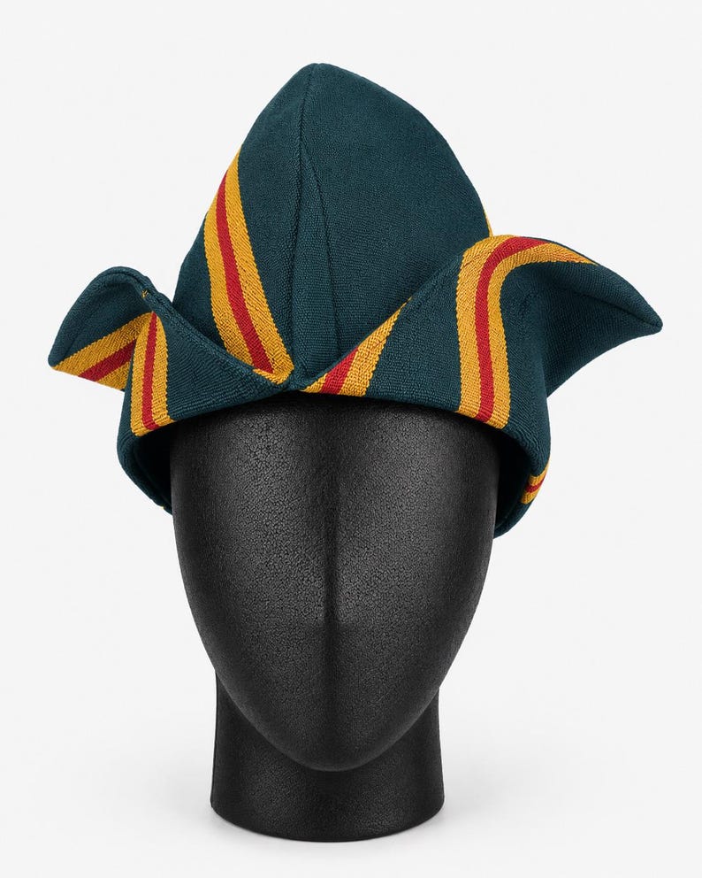 May include: A teal-colored hat with yellow and red stripes. The hat is displayed on a black mannequin head. The hat has a unique shape with pointed top and folded edges. The stripes run vertically along the hat's surface.