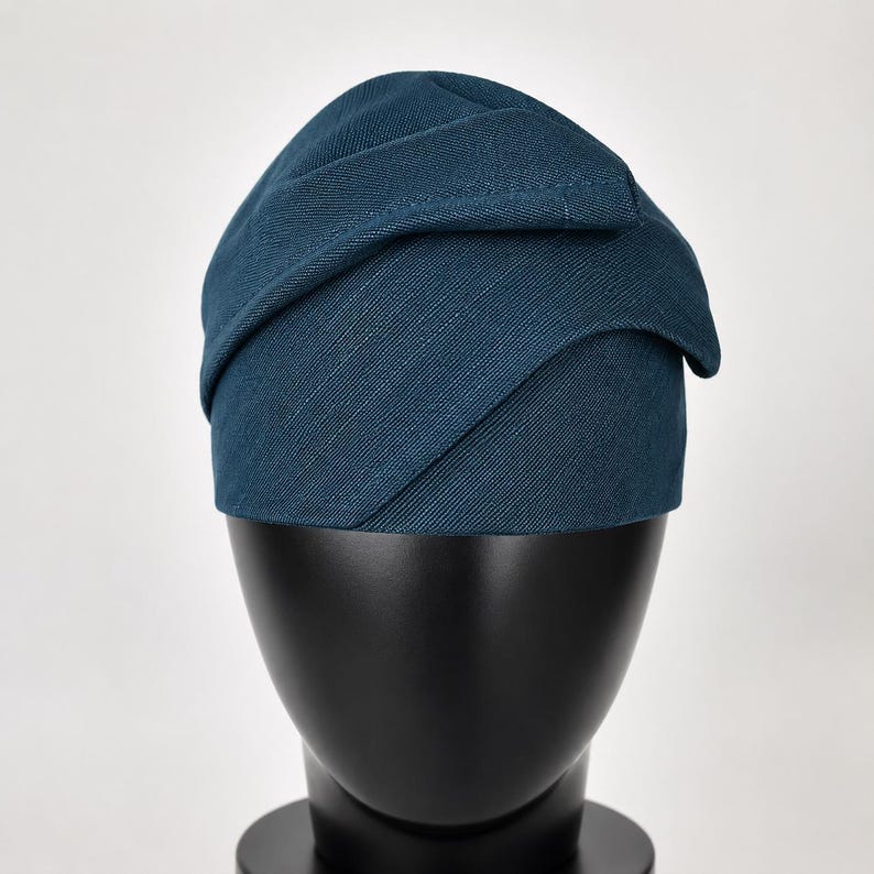 Peut inclure: Un chapeau de couleur sarcelle avec un design superpos&eacute;. Le chapeau est fait d'un tissu textur&eacute; et repose sur une t&ecirc;te de mannequin noire. Le design du chapeau pr&eacute;sente des panneaux de tissu qui se chevauchent, cr&eacute;ant une apparence unique et &eacute;l&eacute;gante. C'est un accessoire de mode.