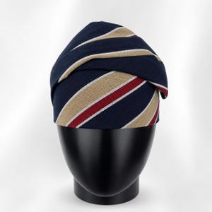 Peut inclure: Un turban ray&eacute; bleu marine et beige avec une rayure rouge et blanche. Le turban est pr&eacute;sent&eacute; sur une t&ecirc;te de mannequin noire.