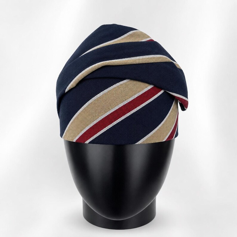 Peut inclure: Un turban ray&eacute; bleu marine et beige avec une rayure rouge et blanche. Le turban est pr&eacute;sent&eacute; sur une t&ecirc;te de mannequin noire.