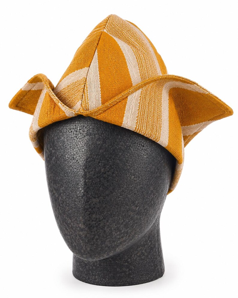 May include: A yellow and white striped hat with a unique folded brim. The hat is displayed on a black mannequin head. The hat's design features a combination of yellow and white vertical stripes, creating a visually appealing pattern. The brim is folded up on the sides.