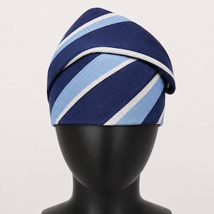 Peut inclure: Un chapeau bleu marine &agrave; rayures blanches et bleu clair. Le chapeau est pr&eacute;sent&eacute; sur une t&ecirc;te de mannequin noire. Le chapeau est un accessoire &eacute;l&eacute;gant. Le design du chapeau rappelle une cravate.