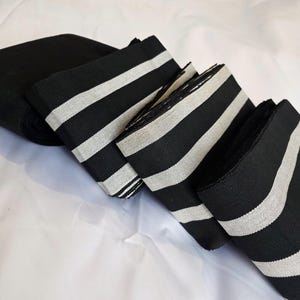 May include: A set of four black and white striped fabric strips. The fabric is folded and stacked, showing the alternating black and white stripes.