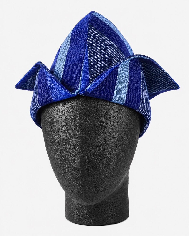 May include: A blue and white striped hat with a unique folded design. The hat is displayed on a black mannequin head. The hat's color scheme includes shades of blue and white, creating a visually appealing accessory.