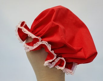 Può includere: Un cappello per la doccia in tessuto rosso con bordo in pizzo bianco. Il cappello è su una testa di manichino rivestita in tessuto.