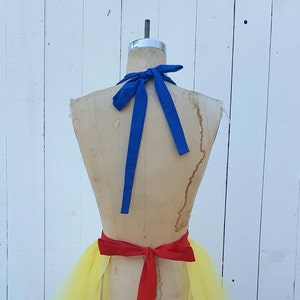May include: A yellow tulle skirt with a red ribbon tied around the waist. A blue ribbon is tied around the neck of the mannequin.