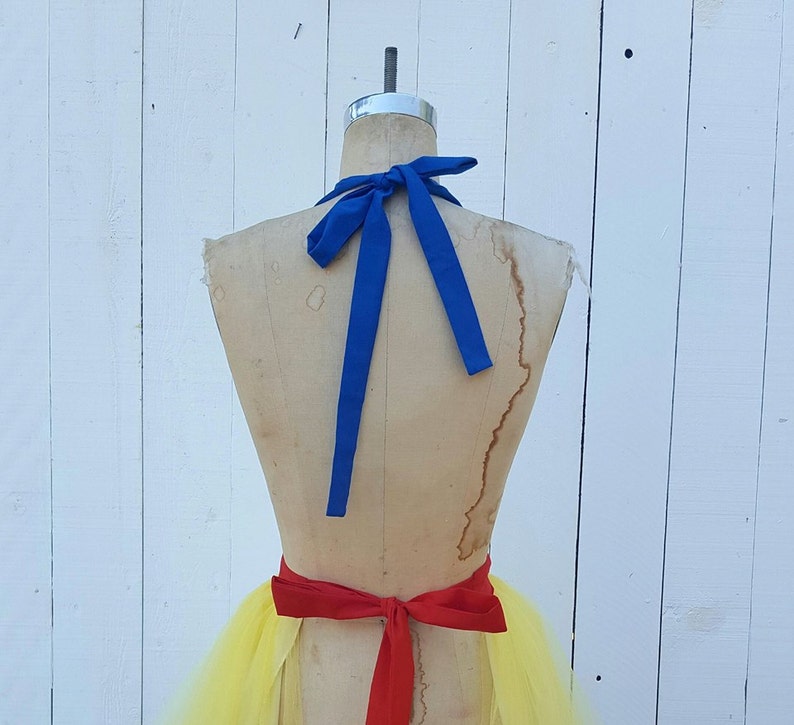 May include: A yellow tulle skirt with a red ribbon tied around the waist. A blue ribbon is tied around the neck of the mannequin.