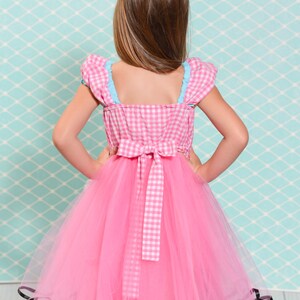May include: A pink tulle dress with a white and pink gingham bodice and black trim. The dress has a bow at the back.