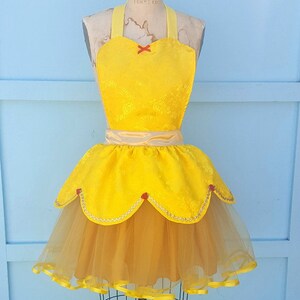 May include: A yellow and gold Belle-inspired apron with a tulle skirt and red accents. The apron has a heart-shaped neckline and a satin sash.