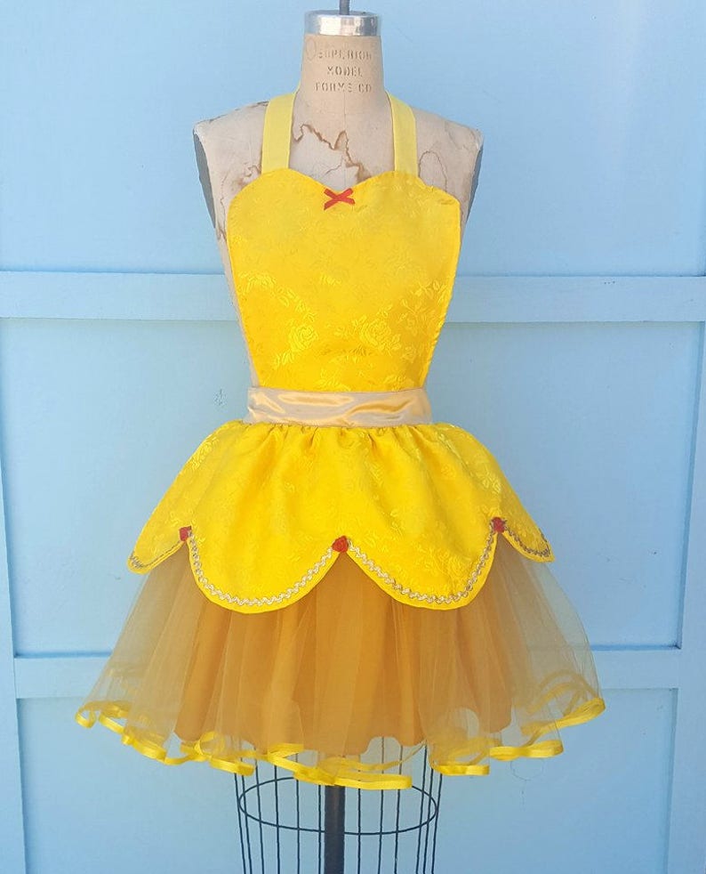 May include: A yellow and gold Belle-inspired apron with a tulle skirt and red accents. The apron has a heart-shaped neckline and a satin sash.