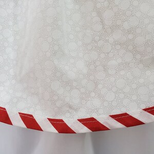 May include: White fabric with a small white polka dot pattern. The fabric has a red and white striped trim.