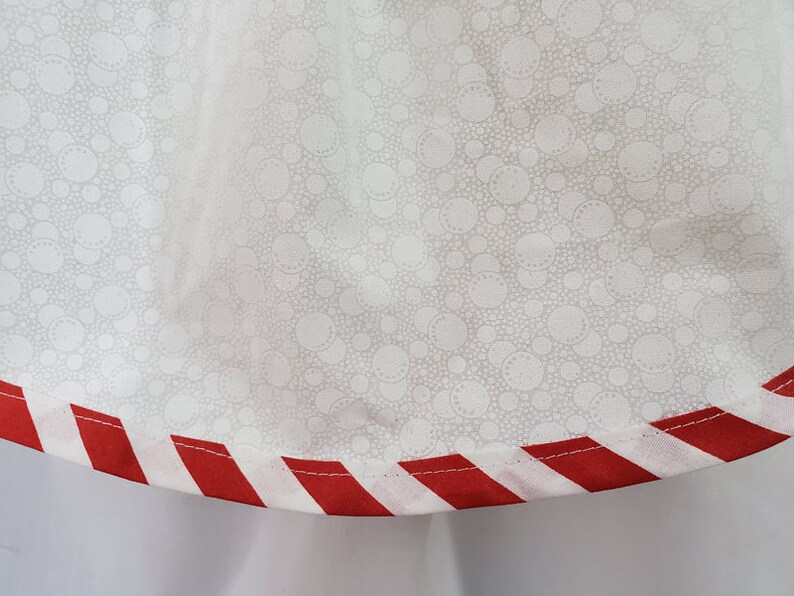 May include: White fabric with a small white polka dot pattern. The fabric has a red and white striped trim.