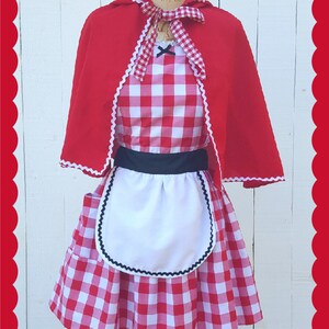 May include: Red and white gingham dress with a white apron and a red hooded cape. The dress has a black belt and black trim on the apron.