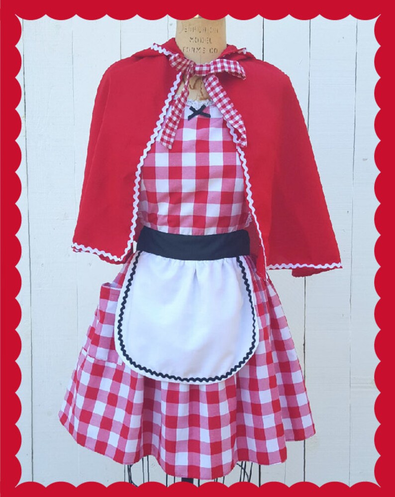 May include: Red and white gingham dress with a white apron and a red hooded cape. The dress has a black belt and black trim on the apron.