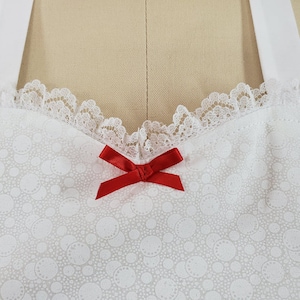 May include: White lace trim with a red bow on a white fabric with a small white dot pattern.