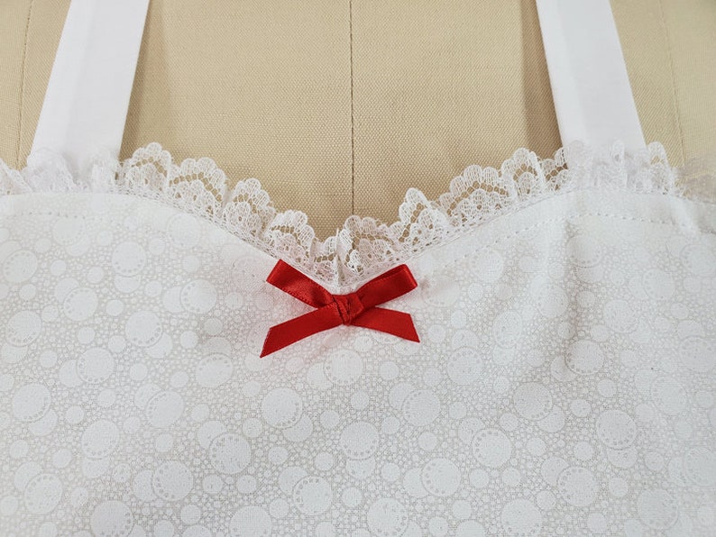 May include: White lace trim with a red bow on a white fabric with a small white dot pattern.