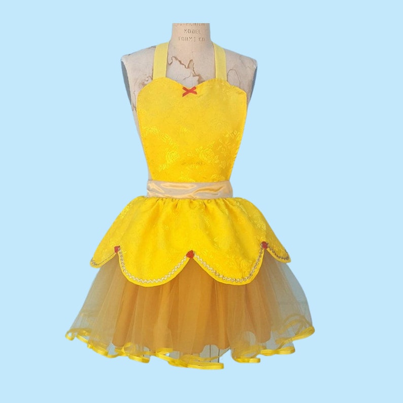 May include: A yellow and gold apron with a tulle skirt. The apron has a sweetheart neckline and a red bow. The skirt is layered with tulle and has a scalloped edge.
