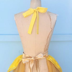 May include: A yellow and gold tulle skirt with a yellow satin bow and matching halter top. The skirt has a ruffled hem and the top has a halter neck style.
