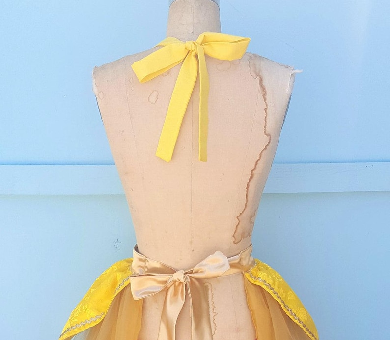 May include: A yellow and gold tulle skirt with a yellow satin bow and matching halter top. The skirt has a ruffled hem and the top has a halter neck style.