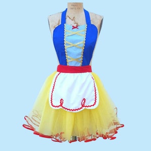 May include: A blue and white apron with a red and white trim and a yellow tulle skirt. The apron has a criss-cross design on the bodice and a red bow at the top.