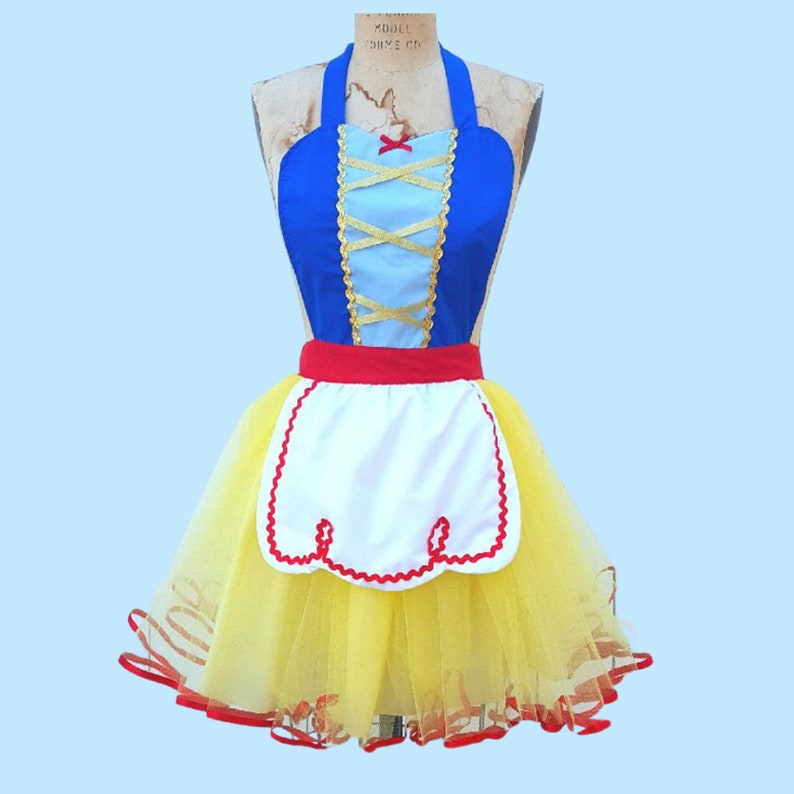 May include: A blue and white apron with a red and white trim and a yellow tulle skirt. The apron has a criss-cross design on the bodice and a red bow at the top.