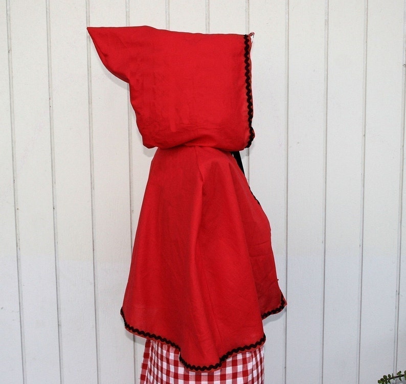 May include: Red hooded cape with black trim. The cape is made of a soft fabric and has a pointed hood.