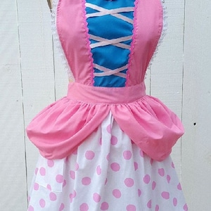 May include: A pink and blue apron with a heart-shaped bodice, white lace trim, and a pink polka dot skirt.
