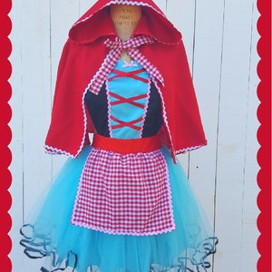 May include: A red hooded cape with white lace trim over a blue tulle skirt with a red and white gingham apron. The skirt has a black lace trim.