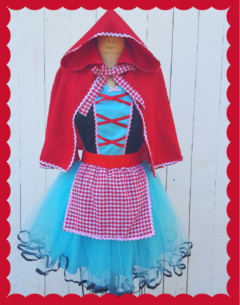 May include: A red hooded cape with white lace trim over a blue tulle skirt with a red and white gingham apron. The skirt has a black lace trim.