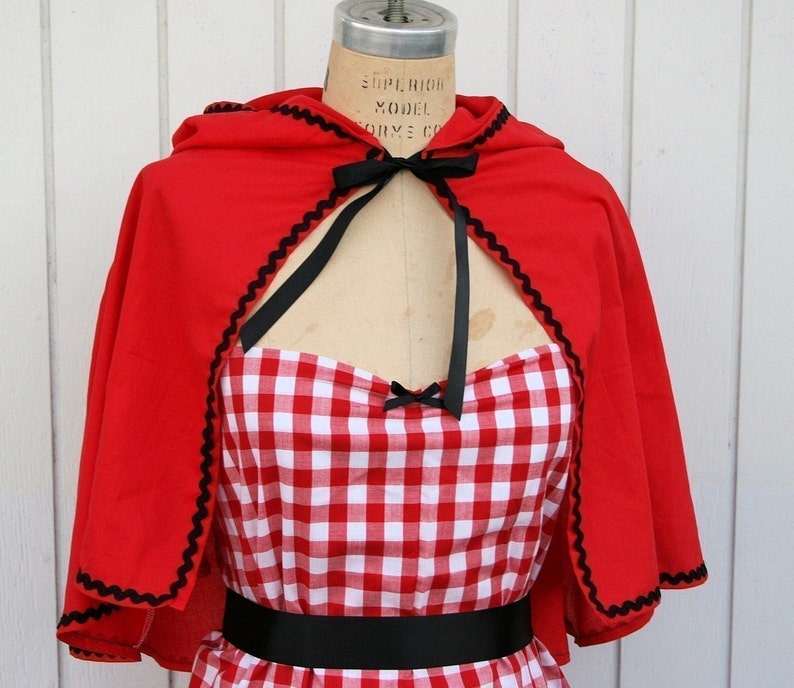 May include: Red hooded cape with black trim and a red and white gingham dress with a black belt.