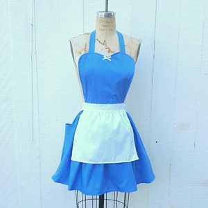 May include: A blue and white apron with a white ruffle trim and a bow at the neckline. The apron is on a dress form.